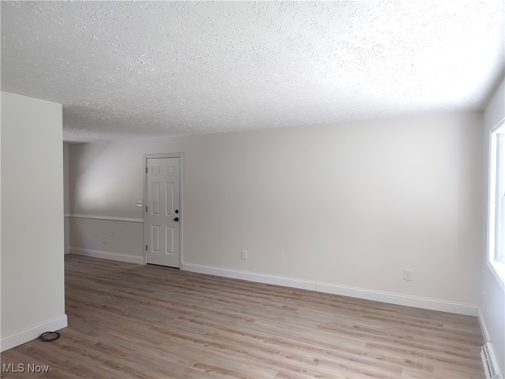 8016 Ninevah Road Geneva, OH 44041 - Photo 15 of 45 Spare room with light wood-style floors, a textured ceiling, healthy amount of natural light, and a baseboard heating unit