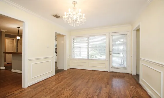 an empty room with wooden floor chandelier and windows