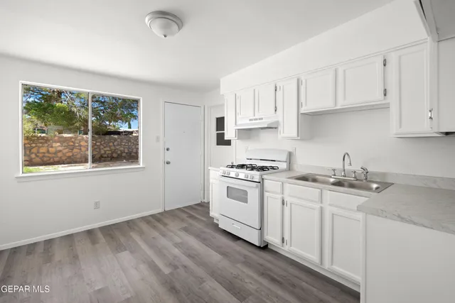 a kitchen with stainless steel appliances granite countertop a stove a sink dishwasher and white cabinets with wooden floor