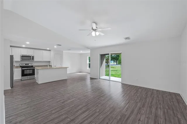 a view of an empty room and kitchen with wooden floor and a kitchen