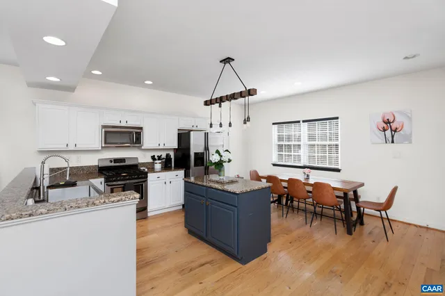 a kitchen with stainless steel appliances granite countertop a stove top oven a sink dishwasher a dining table and chairs with wooden floor