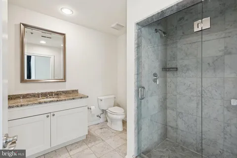 a bathroom with a granite countertop toilet a sink a mirror and shower