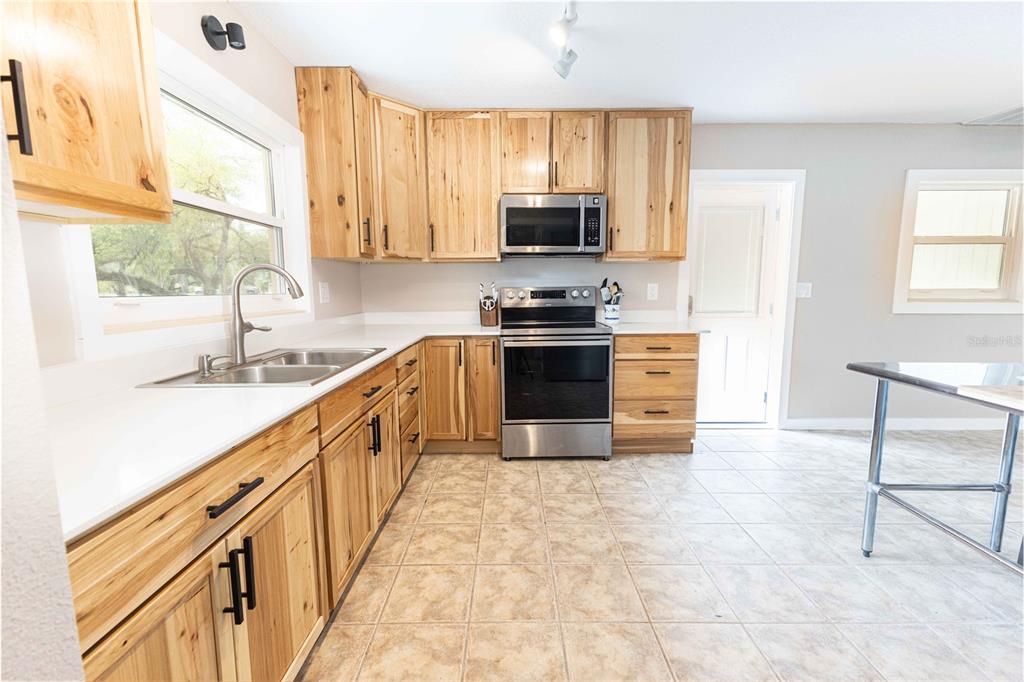 5175 Azalea Circle Dade City, FL 33523 - Photo 3 of 34 a large kitchen with stainless steel appliances granite countertop a stove top oven a sink a dining table and chairs with wooden floor