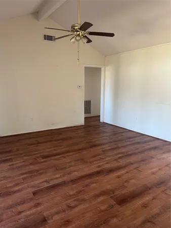 a view of an empty room with wooden floor and a ceiling fan