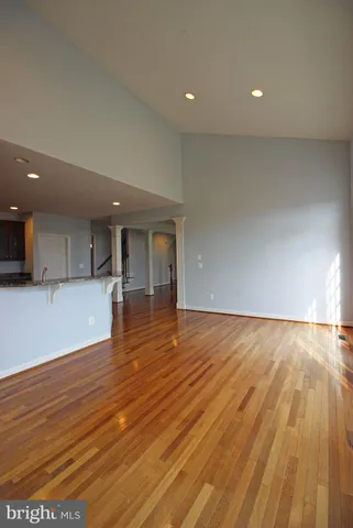 a view of empty room with wooden floor and kitchen
