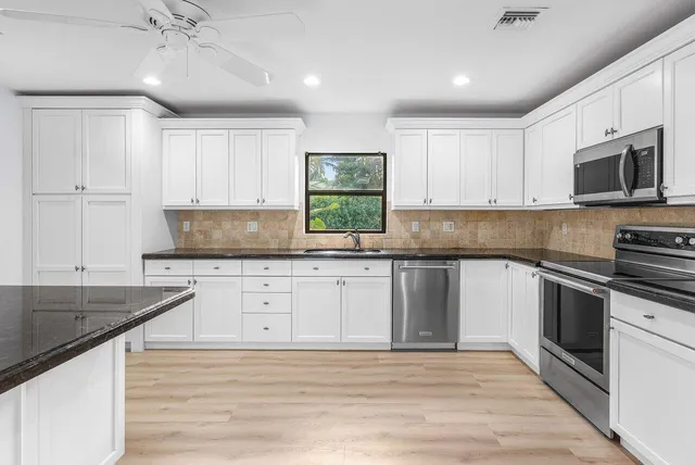 a kitchen with granite countertop white cabinets white appliances a sink and a large window