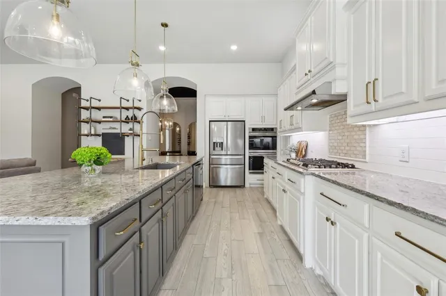 a large kitchen with stainless steel appliances kitchen island granite countertop a large stove a sink dishwasher and white cabinets with wooden floor