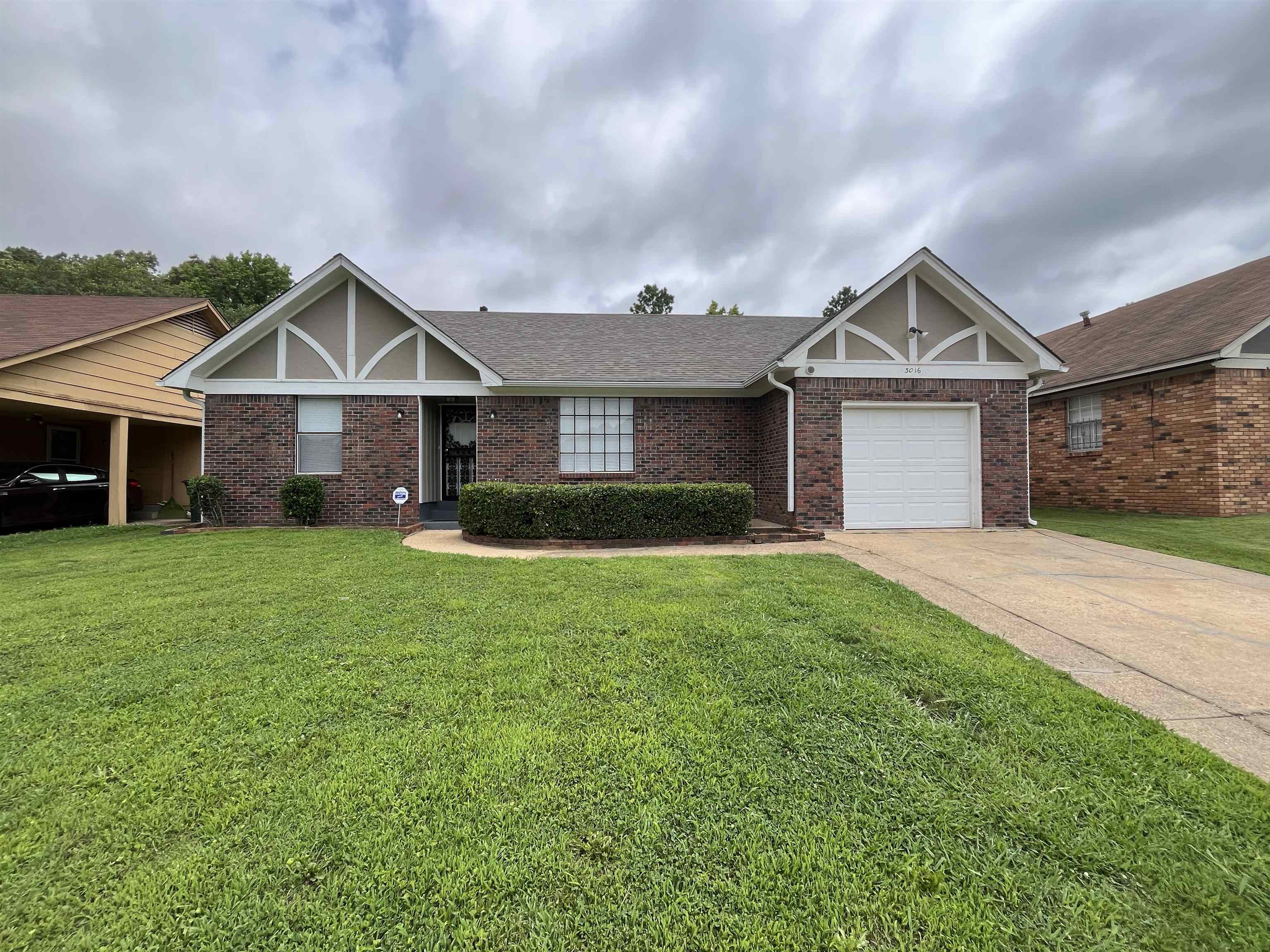 Tudor home with concrete driveway, a front yard, an attached garage, brick siding, and roof with shingles
