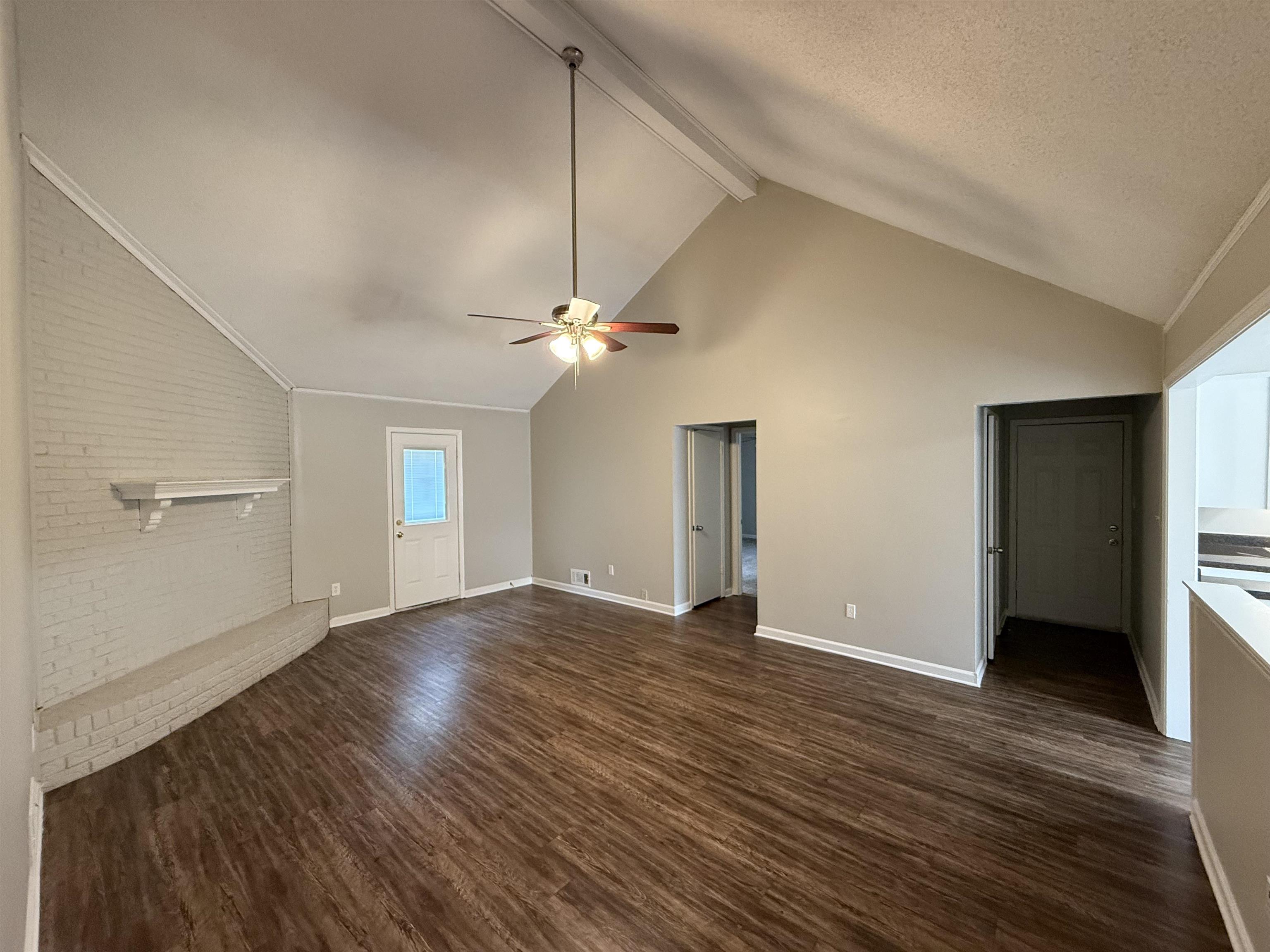 Unfurnished living room featuring dark wood-type flooring, ceiling fan, brick wall, and a textured ceiling