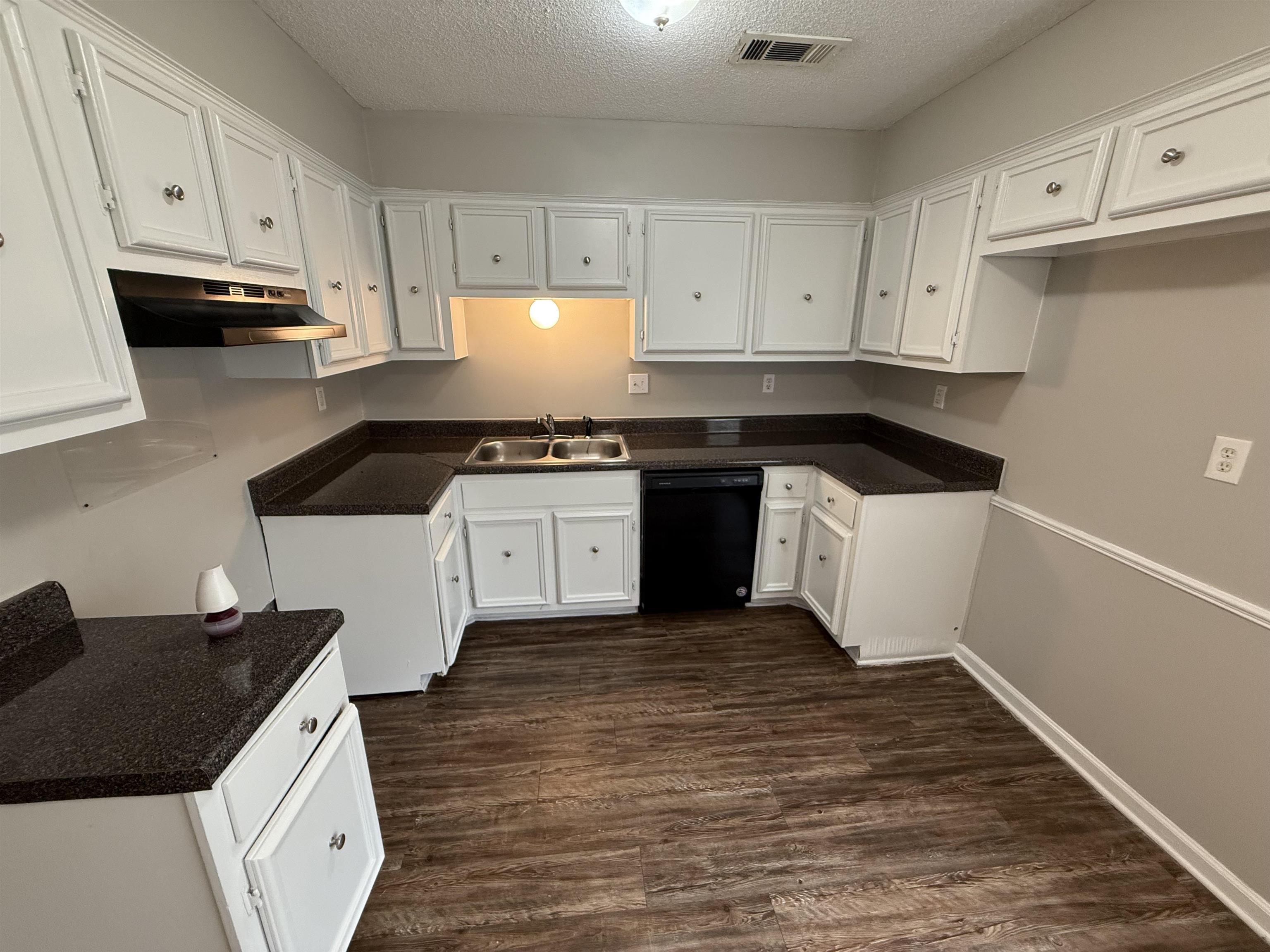 Kitchen featuring black dishwasher, under cabinet range hood, a textured ceiling, dark wood-style floors, and white cabinets