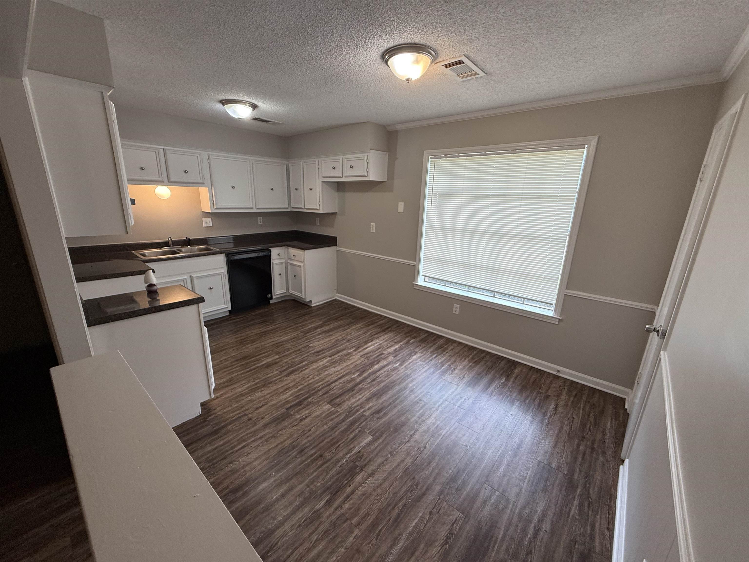 Kitchen with dishwasher, dark countertops, a textured ceiling, dark wood-style floors, and crown molding