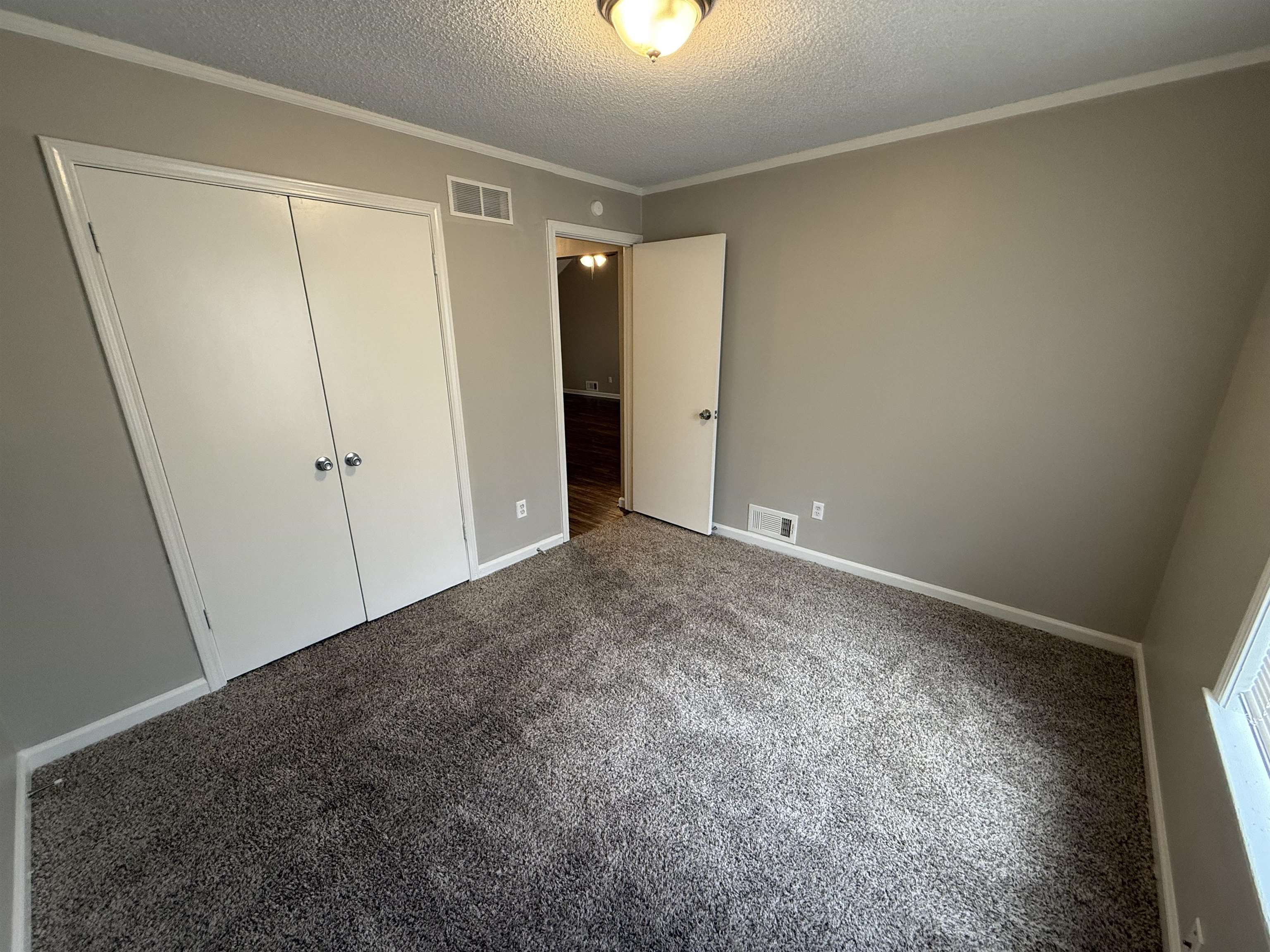 Unfurnished bedroom featuring a textured ceiling, carpet, a closet, and ornamental molding