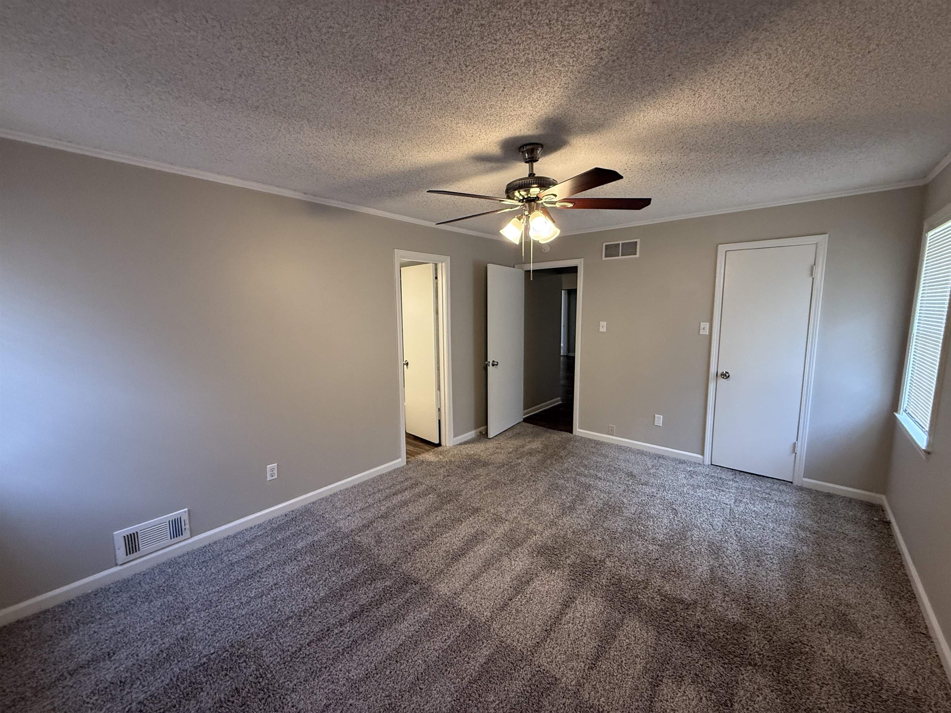 Unfurnished bedroom featuring carpet flooring, ornamental molding, a textured ceiling, and ceiling fan