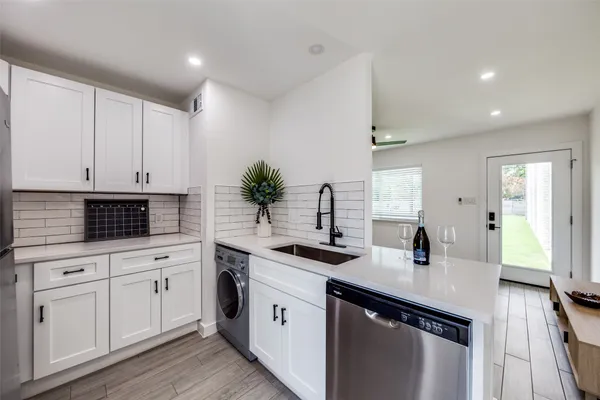 a kitchen with a sink dishwasher stove and white cabinets with wooden floor