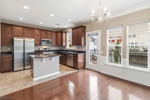 a kitchen with stainless steel appliances granite countertop a refrigerator a sink a stove top oven a large window with wooden floor and cabinets