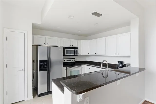 a kitchen with stainless steel appliances granite countertop a sink a microwave a refrigerator and white cabinets
