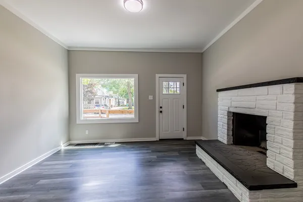 an empty room with wooden floor fireplace and windows