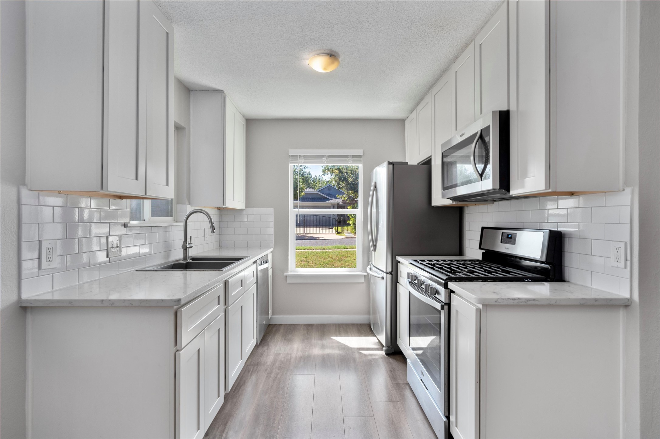 12321 Emery Oaks Road Austin, TX 78758 - Photo 8 of 27 A galley kitchen with light wood-style flooring, white cabinetry, and stainless steel appliances awaits culinary endeavors.