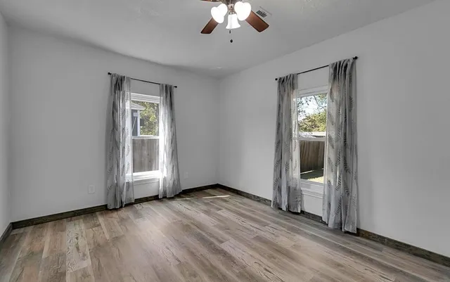 an empty room with wooden floor mirror and windows