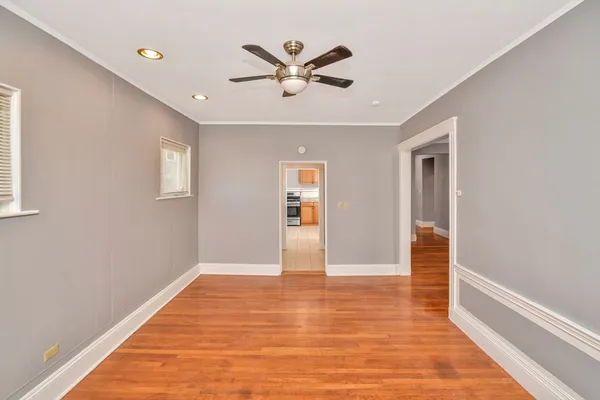 a view of an empty room with wooden floor and a ceiling fan