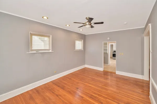 a view of an empty room with wooden floor and a ceiling fan