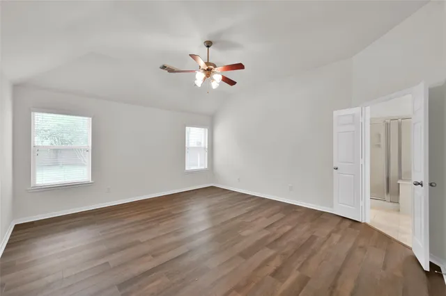 an empty room with wooden floor fan and windows