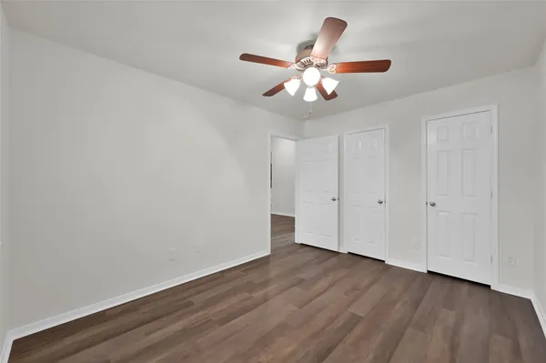 a view of an empty room with wooden floor and a chandelier fan