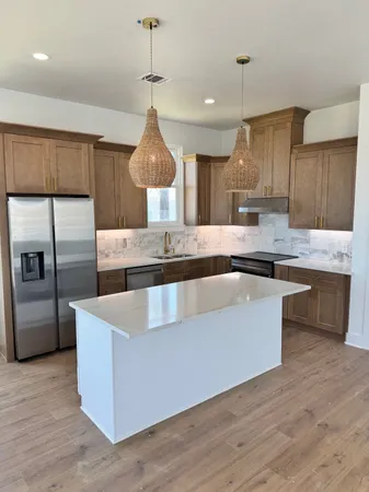 a kitchen with stainless steel appliances granite countertop a sink a stove a refrigerator and island with wooden floor