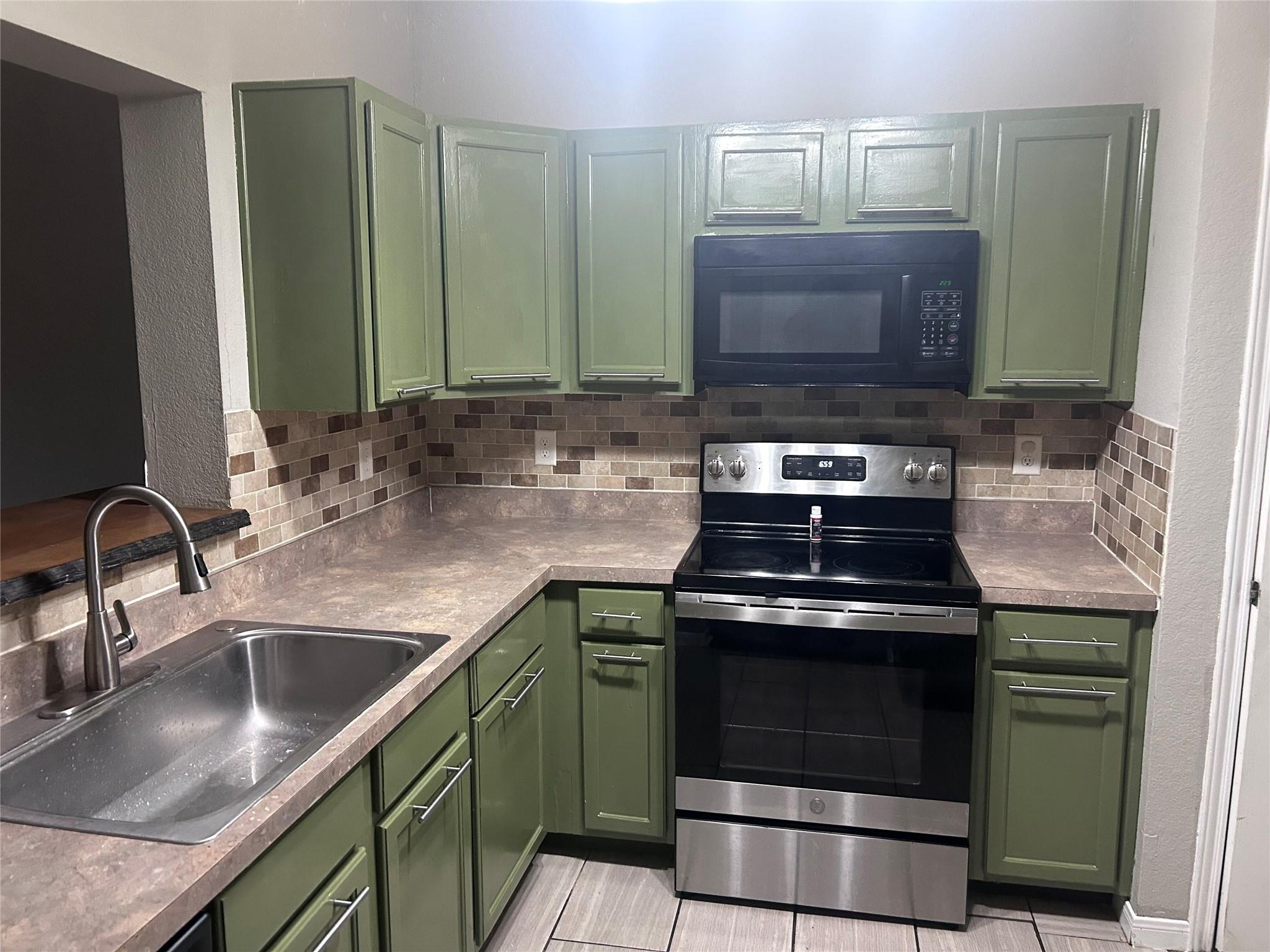 5708 Spring Meadow Road, Unit B Austin, TX 78744 - Photo 2 of 23 Kitchen featuring green cabinetry, stainless steel electric range oven, black microwave, a textured wall, and tasteful backsplash