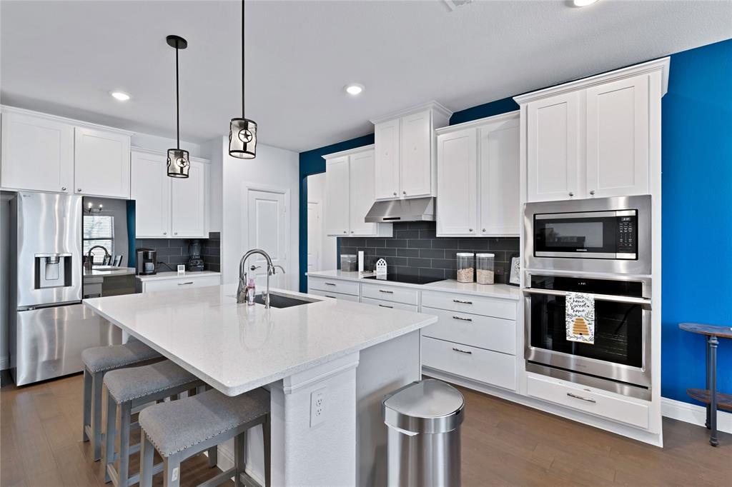 137 Gardenia Drive Azle, TX 76020 - Photo 2 of 38 Kitchen featuring stainless steel appliances, white cabinets, light stone counters, a center island with sink, and dark wood-type flooring