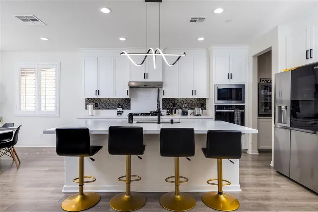 a kitchen with stainless steel appliances a stove a sink a refrigerator and white cabinets with wooden floor