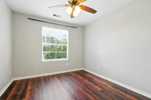 a view of an empty room with wooden floor and a ceiling fan