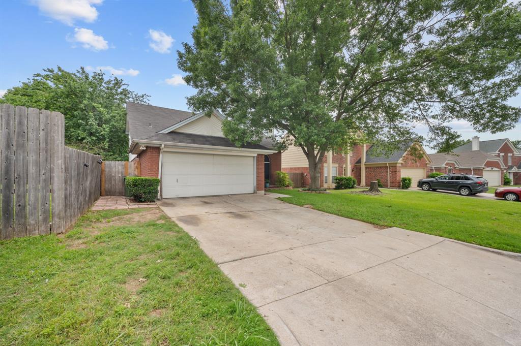 Brick-front home featuring an attached two-car garage with a white door, a sloped shingle roof, and established landscaping