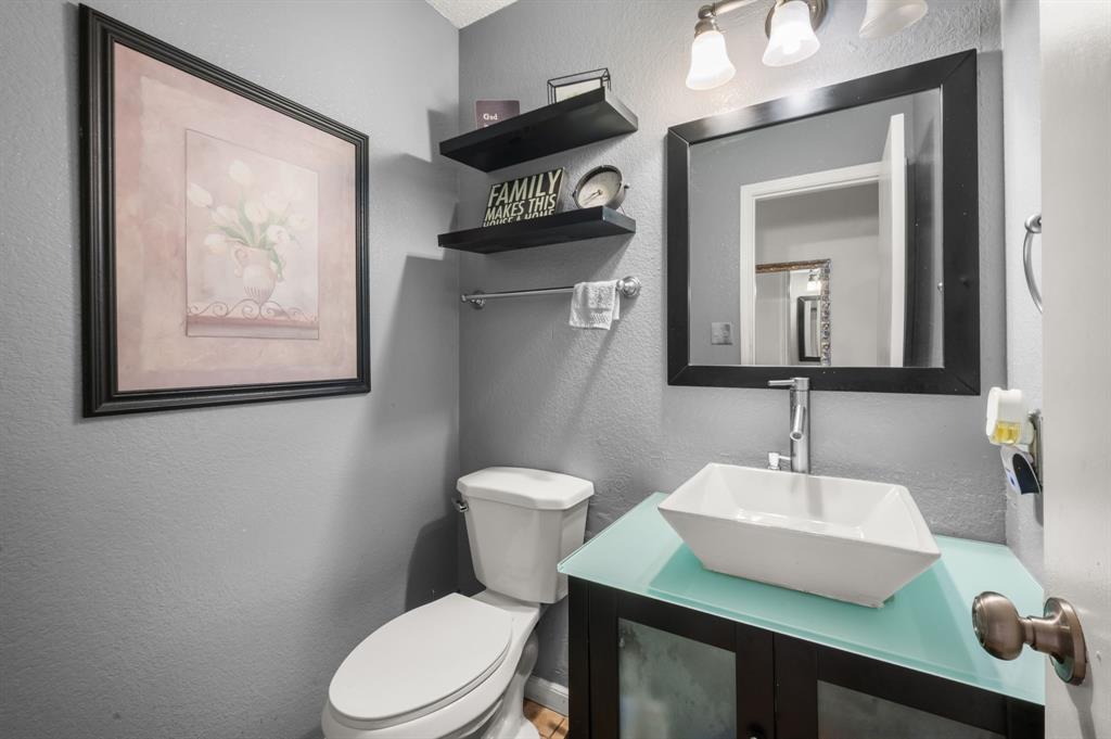 916 Danforth Place Arlington, TX 76017 - Photo 21 of 30 Powder room featuring a vessel sink, frosted glass countertop, wood-finish vanity with frosted glass cabinet doors, and a wall-mounted mirror with a black frame