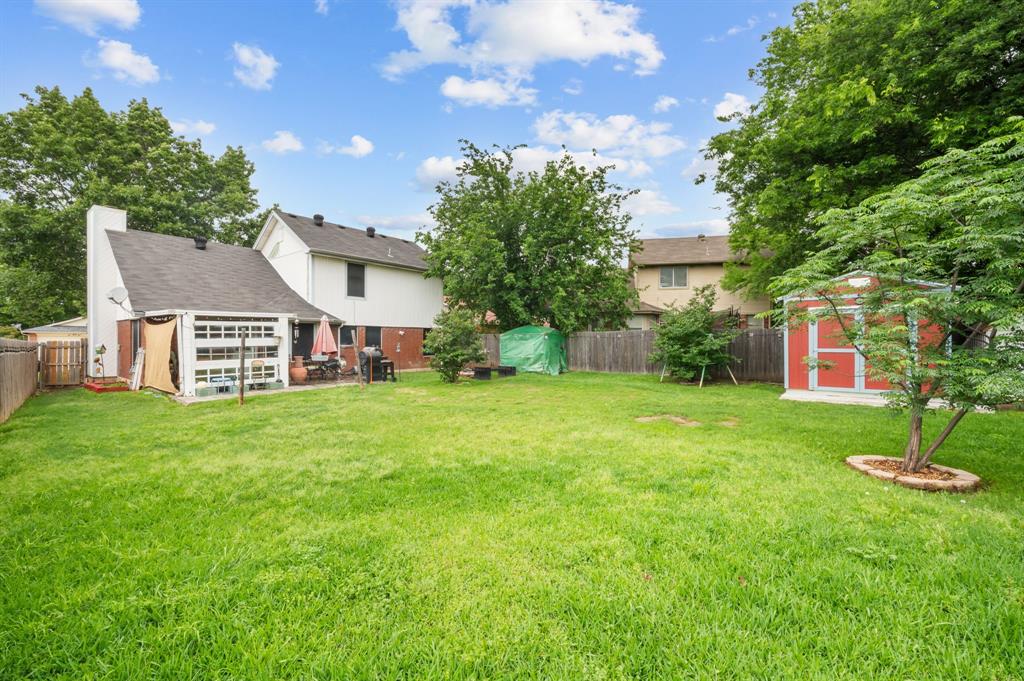 916 Danforth Place Arlington, TX 76017 - Photo 28 of 30 Spacious rear yard featuring a large expanse of green lawn, a red storage shed, mature perimeter trees, and a wooden privacy fence