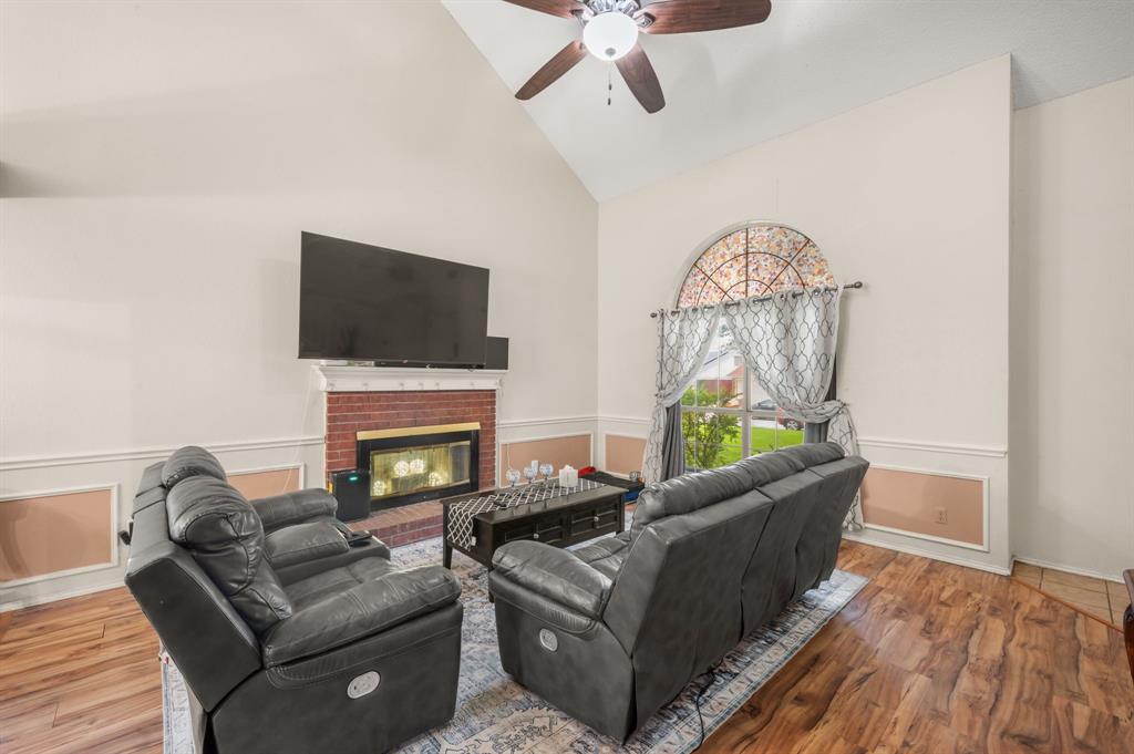 916 Danforth Place Arlington, TX 76017 - Photo 6 of 30 Living room featuring a vaulted ceiling with a ceiling fan, brick-faced fireplace with a mantel, and wood-finish flooring