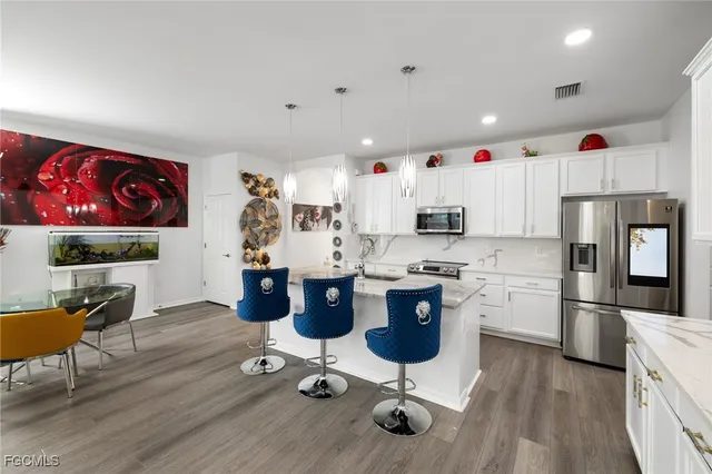 a kitchen with stainless steel appliances kitchen island granite countertop a refrigerator oven a sink dishwasher and white cabinets with wooden floor