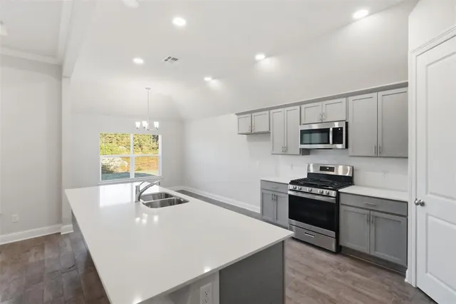 a kitchen with stainless steel appliances granite countertop a sink a stove a microwave a refrigerator with white cabinets and wooden floor