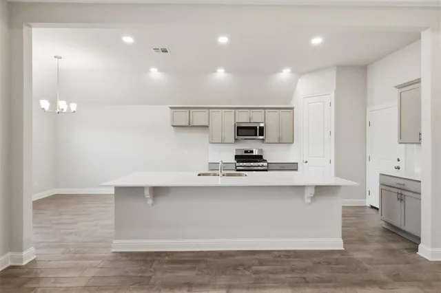 a large white kitchen with stainless steel appliances granite countertop a stove a sink a refrigerator and white cabinets with wooden floor