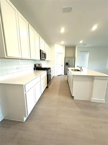 a kitchen with stainless steel appliances granite countertop a stove top oven a sink a refrigerator and white cabinets