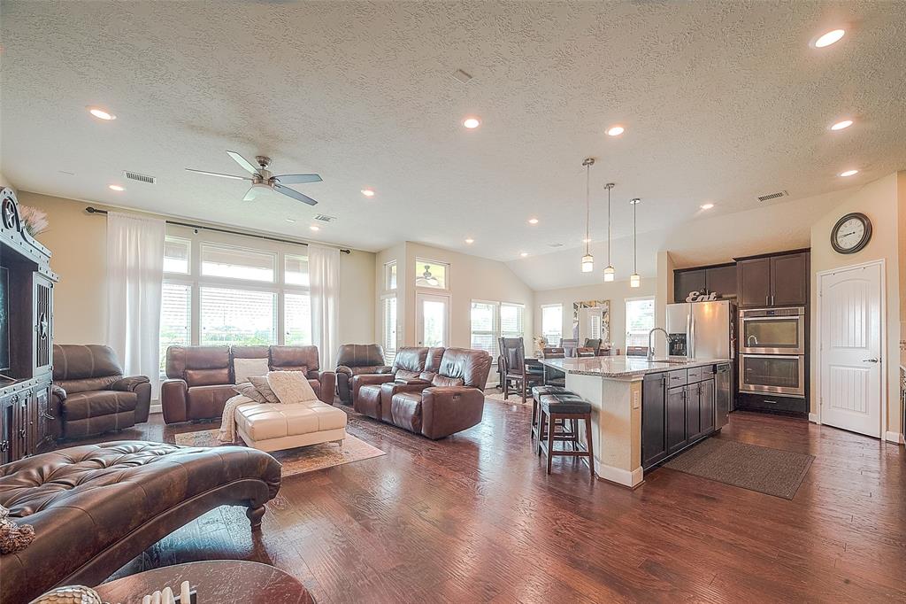 a living room with stainless steel appliances furniture wooden floor and a kitchen view