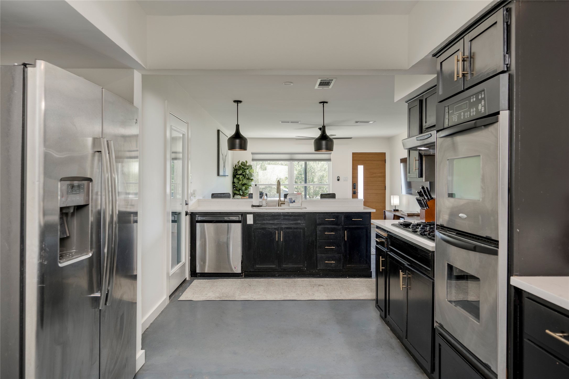 3606 Wilson Street Austin, TX 78704 - Photo 9 of 34 Kitchen with stainless steel appliances, finished concrete flooring, dark cabinets, pendant lighting, and a peninsula