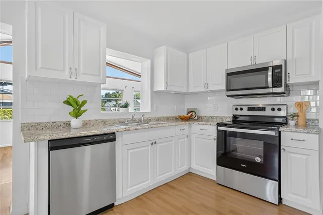 a kitchen with granite countertop a sink stainless steel appliances and white cabinets