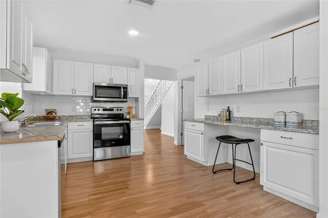 a kitchen with granite countertop a stove top oven a sink dishwasher and a refrigerator with wooden floor