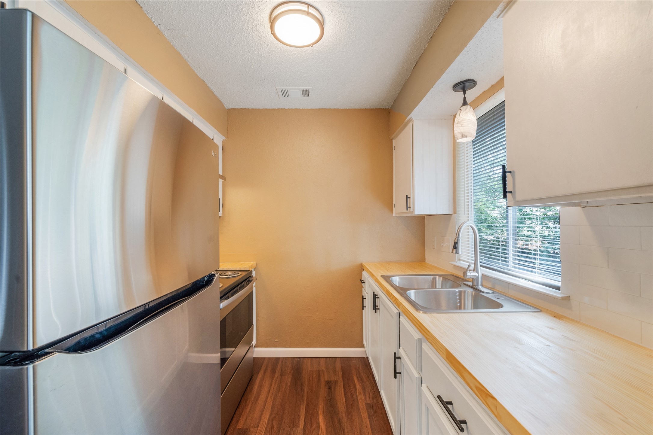 5412 Atascosa Drive, Unit B Austin, TX 78744 - Photo 6 of 15 Kitchen featuring appliances with stainless steel finishes, white cabinets, light countertops, dark wood-style flooring, and a textured ceiling