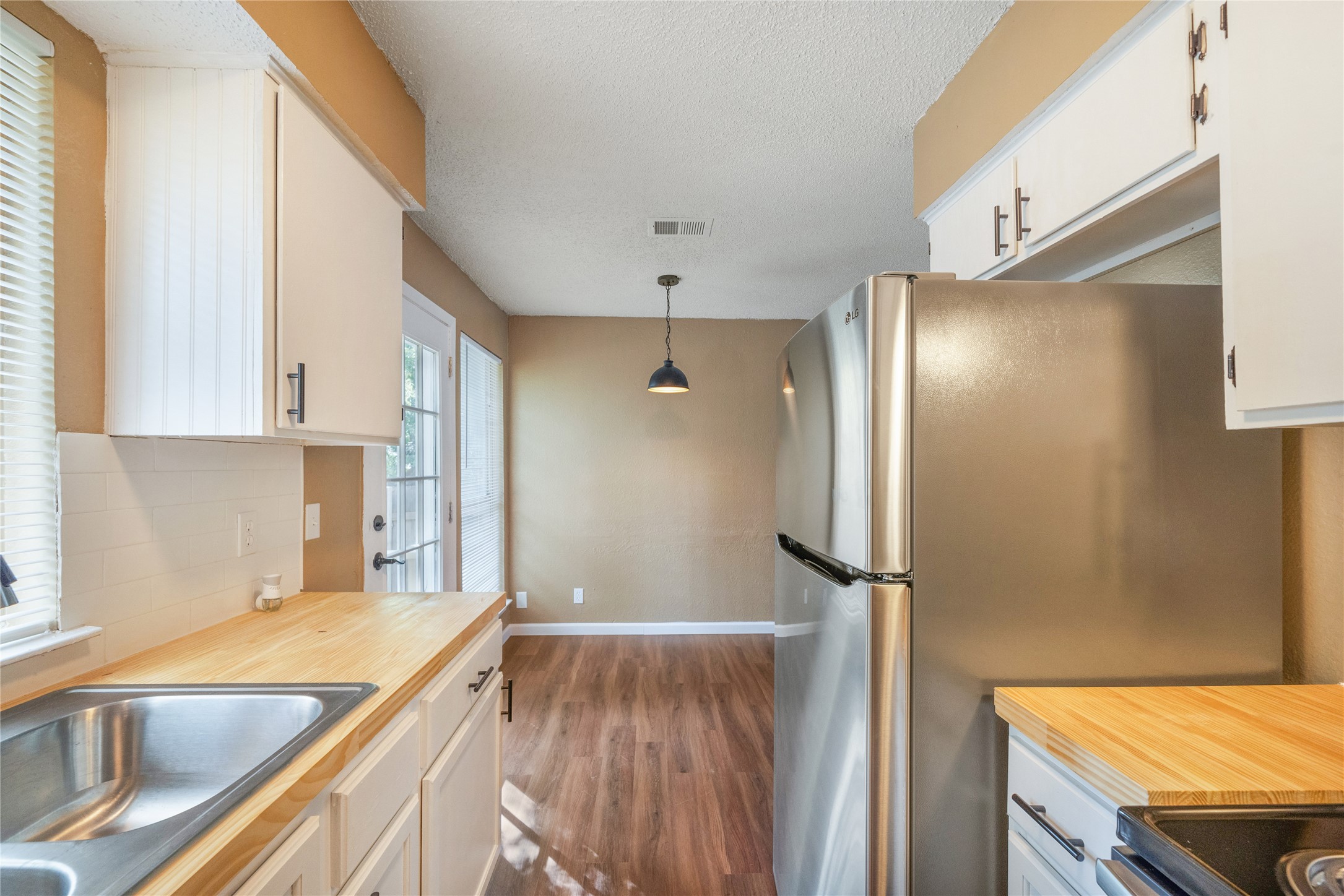 5412 Atascosa Drive, Unit B Austin, TX 78744 - Photo 7 of 15 Kitchen featuring decorative light fixtures, white cabinets, light countertops, dark wood-style floors, and a textured ceiling