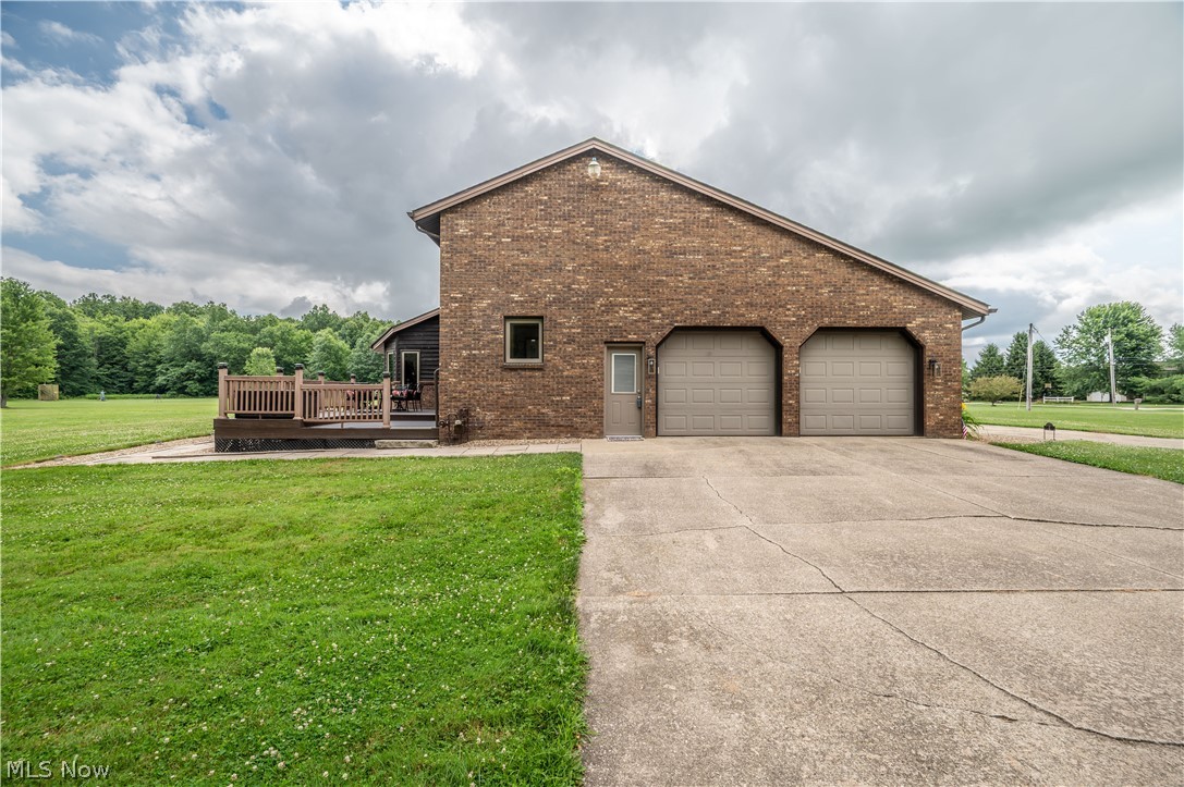 405 Airport Road Northwest Warren, OH 44481 - Photo 40 of 50 Brick exterior featuring a two-car garage with arched entrances, a concrete driveway, and a wood-deck patio
