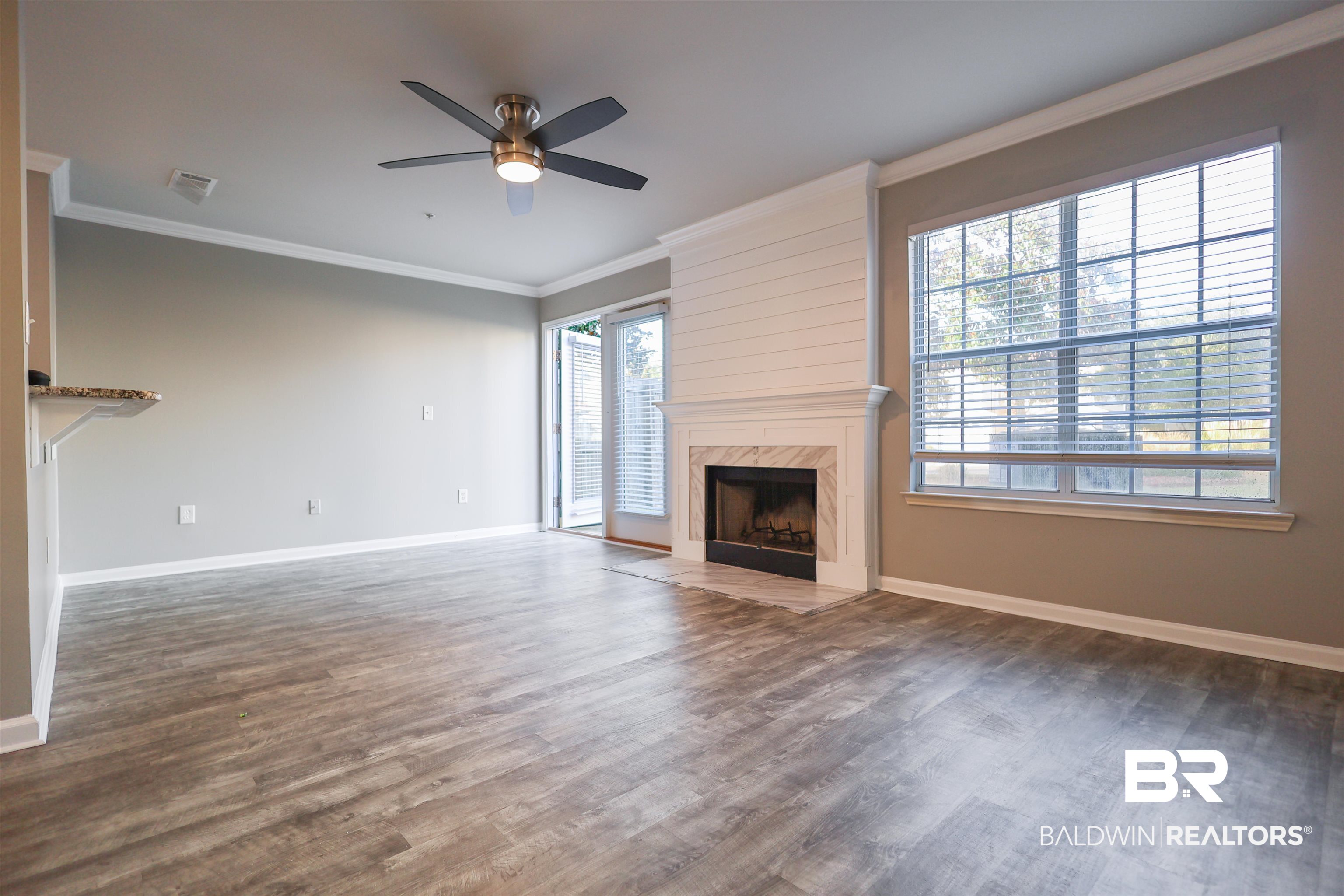 1517 Regency Road, Unit 125 Gulf Shores, AL 36542 - Photo 6 of 26 Unfurnished living room with crown molding, a high end fireplace, dark wood-style floors, and a ceiling fan
