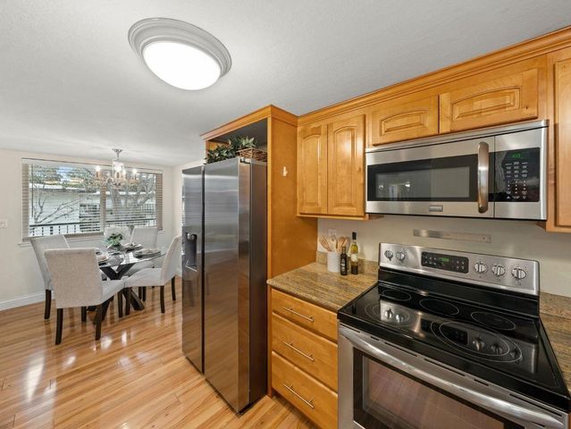 a kitchen with stainless steel appliances a stove a sink dishwasher a refrigerator cabinets and a dining table with wooden floor