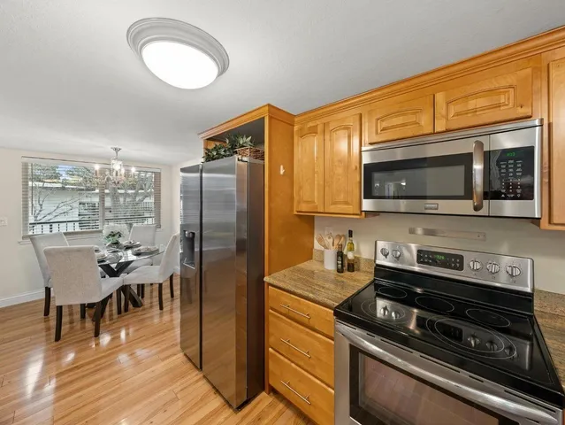 a kitchen with stainless steel appliances a stove a sink dishwasher a refrigerator cabinets and a dining table with wooden floor